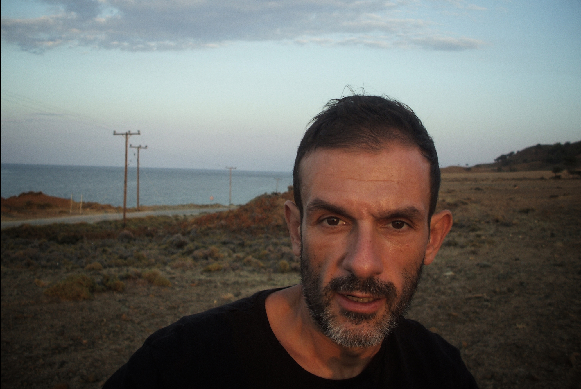 close up of Greek artist Larry Gus, with natural landscape in the background 